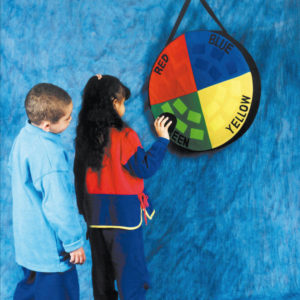 Um menino e uma menina estão em pé, em frente ao painel do Bug-Ball. Ela tem na mão direita, uma bolinha preta, que aproxima do velcro verde do painel.